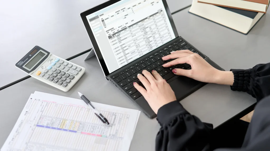 Person performing manual data entry into spreadsheets with calculator and notes on desk