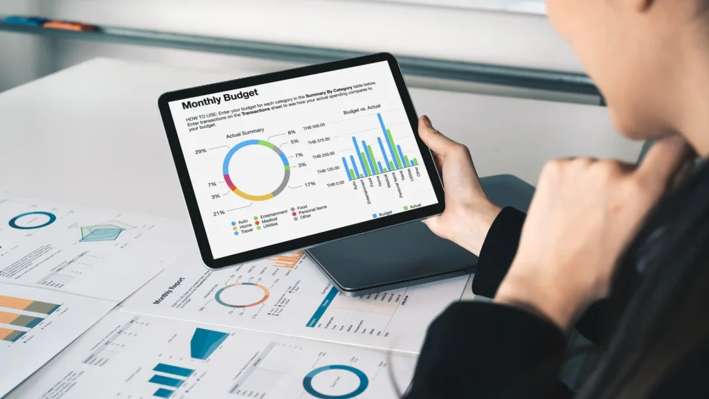 Business professional reviewing candlestick chart on tablet with printed financial reports and analytics data