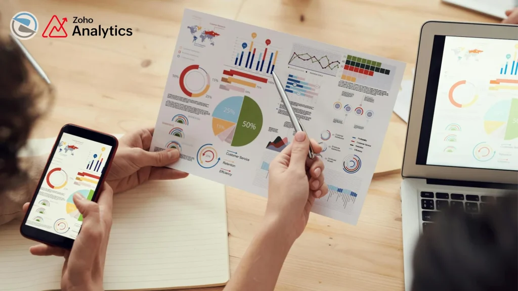Hands analyzing colorful Zoho Analytics dashboards on laptop tablet and phone showing clear data insights